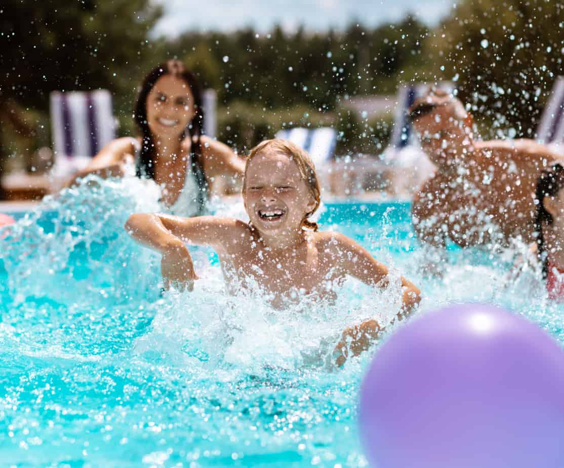 Two adults and two children splashing around in a pool with a big purple ball.